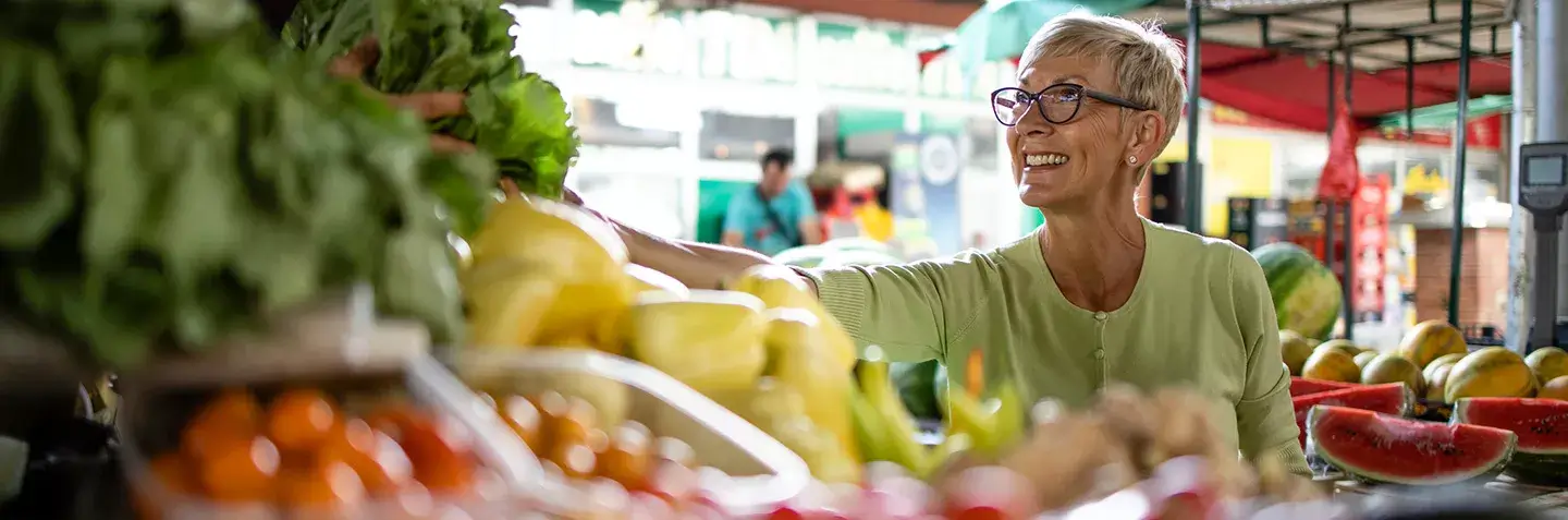 A smiling woman choosing fresh vegetables at a food market stall.